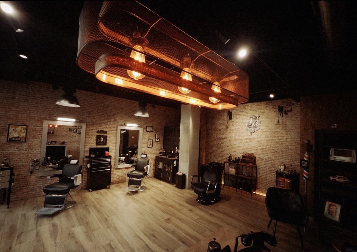 Interior de SCR Barber en Tarragona con sillones de barbero clásicos, lámpara industrial de cobre y paredes de ladrillo visto