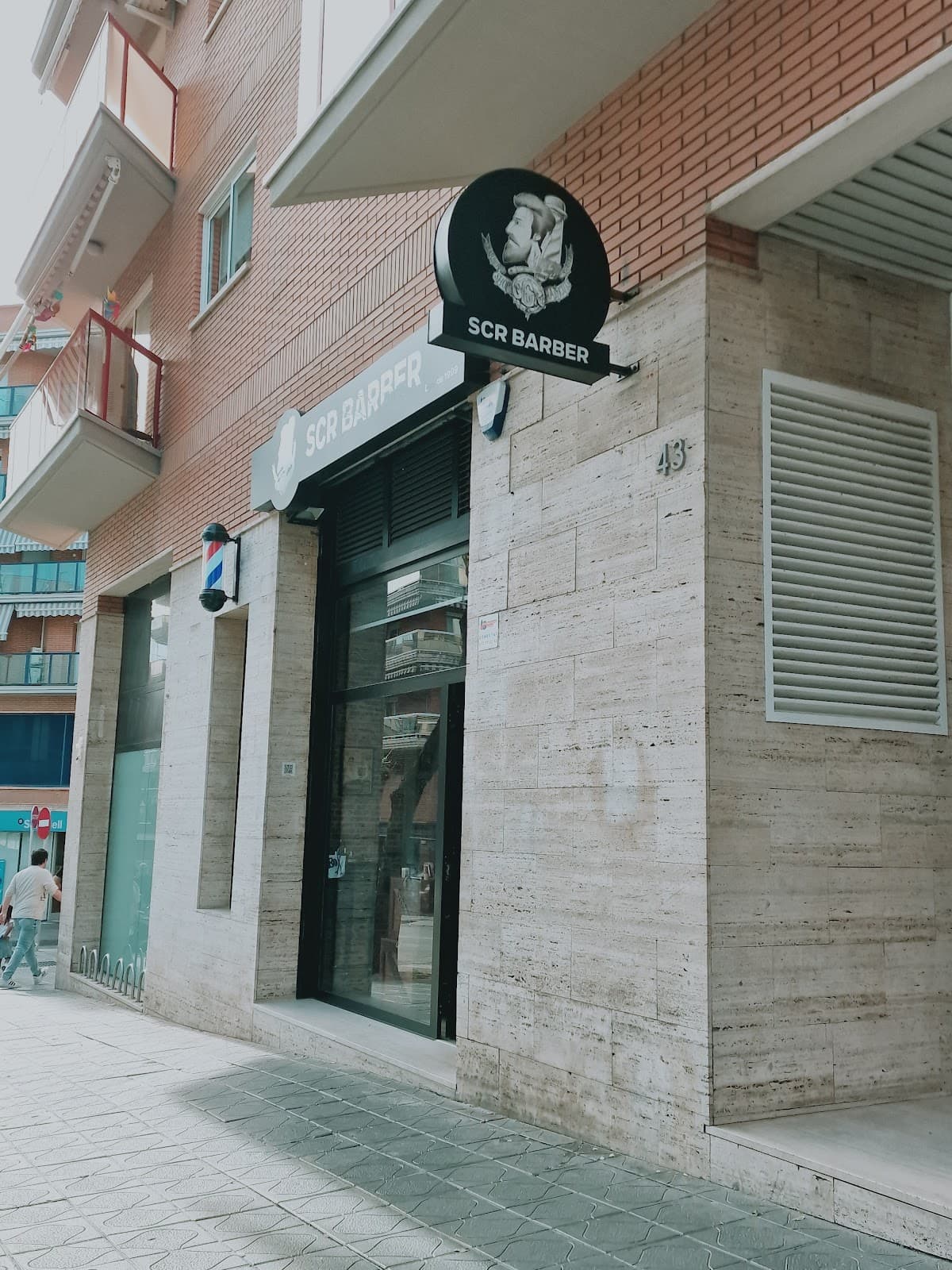 Fachada de SCR Barber en Tarragona con el rótulo circular de la marca y el poste de barbero clásico en la entrada